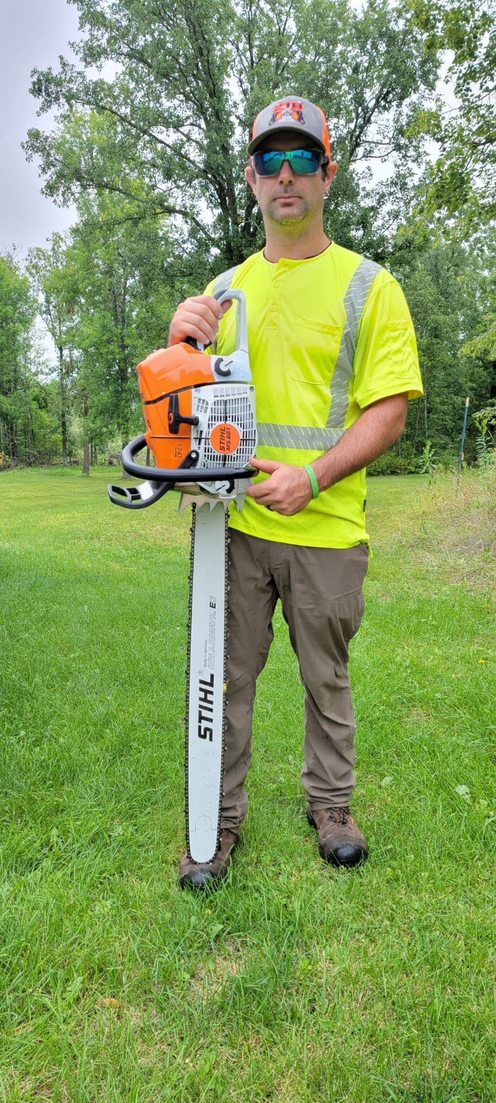 Man in safety gear holding a STIHL chainsaw in a green outdoor setting.