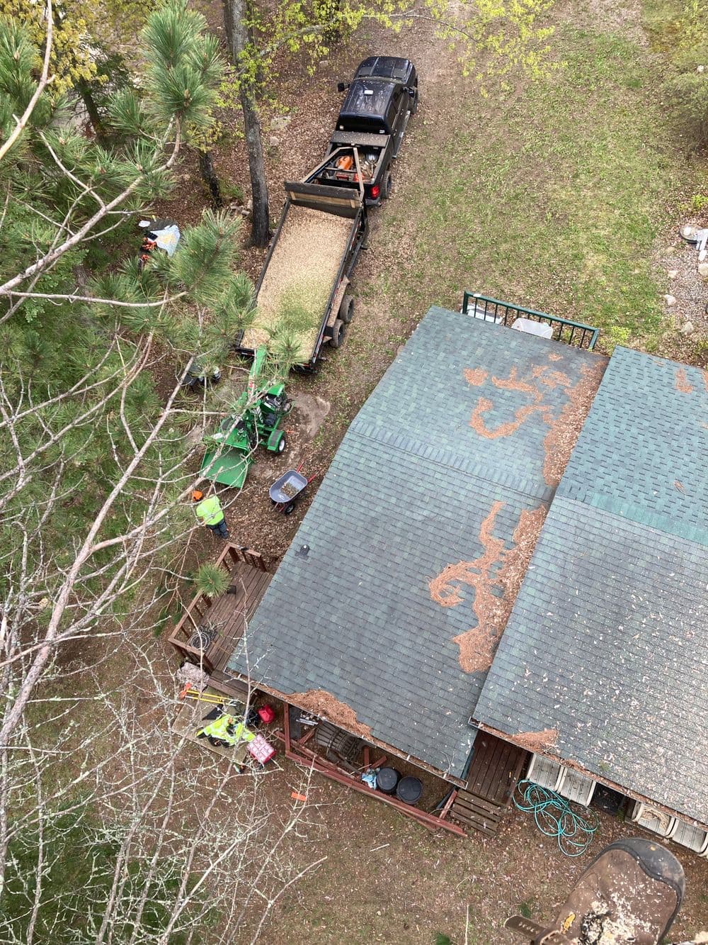 Aerial view of a cabin with a pickup truck unloading gravel and various outdoor equipment nearby.